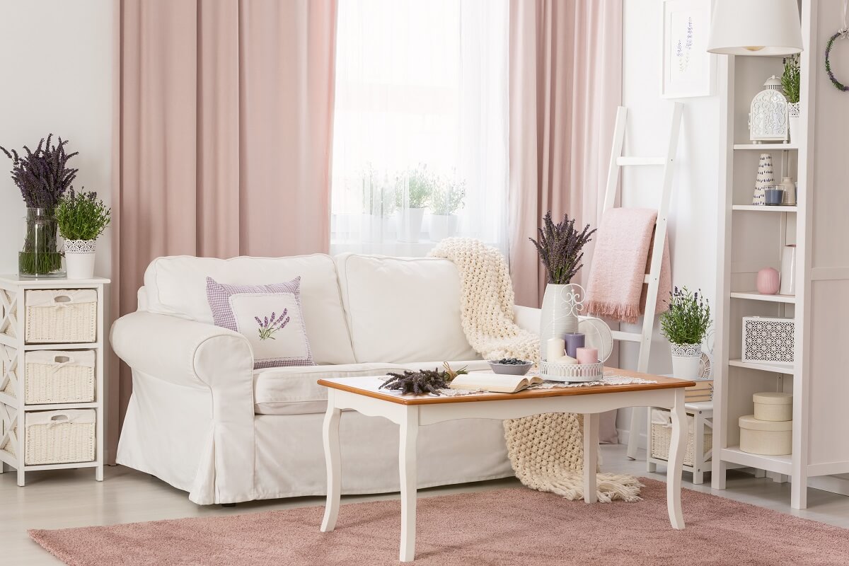 Biała sofa, stolik z drewnianym blatem i lawenda w salonie w stylu prowansalskim