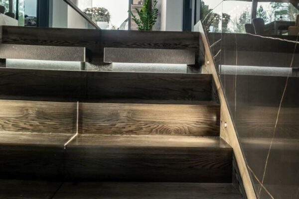 Drewniane schody z podświetlanymi stopniami i szklaną balustradą