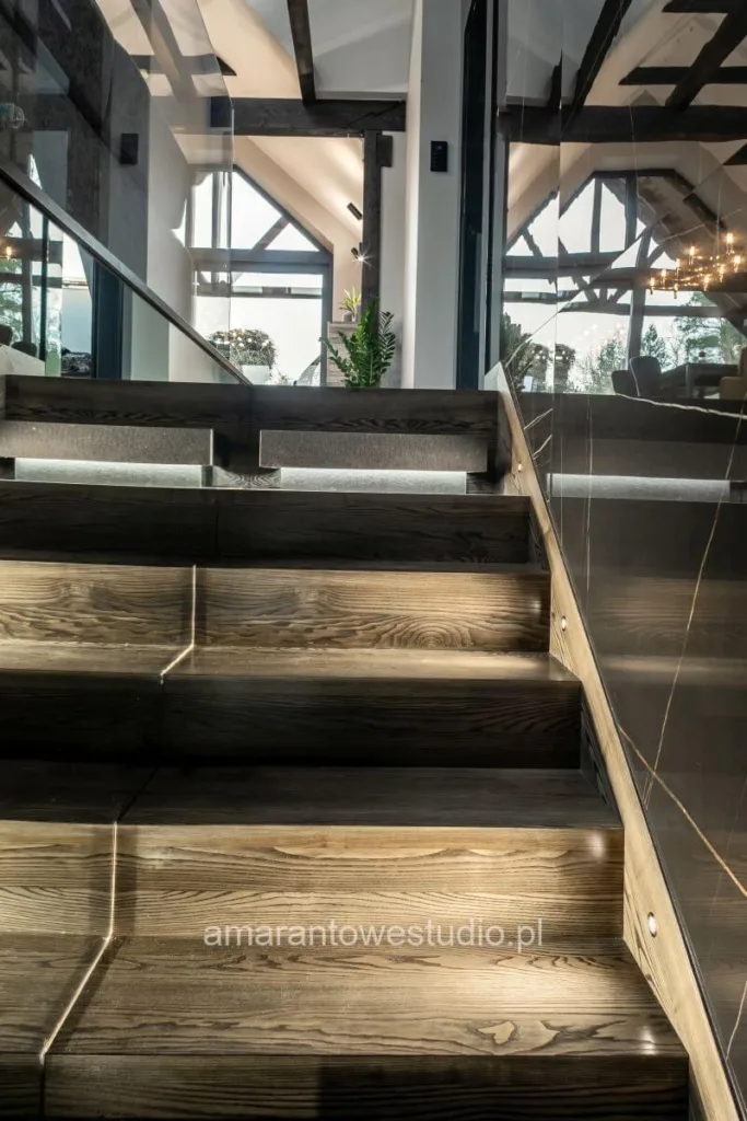 Drewniane schody z podświetlanymi stopniami i szklaną balustradą