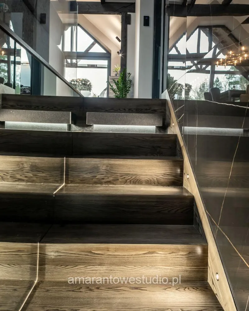 Drewniane schody z podświetlanymi stopniami i szklaną balustradą