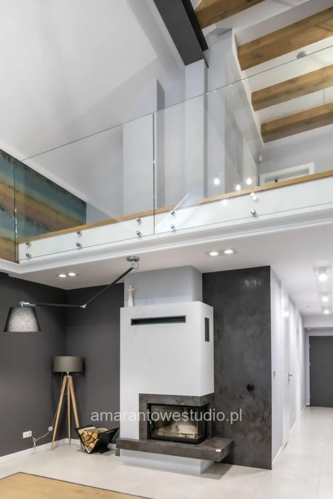 Salon z kominkiem pod antresolą ze szklaną balustradą