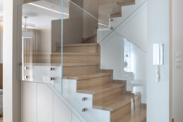 Schody z drewnianymi stopniami, szklaną balustradą i szafami pod spodem