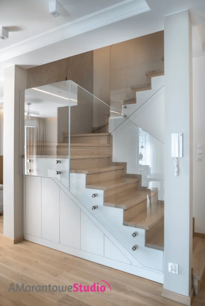 Schody z drewnianymi stopniami, szklaną balustradą i szafami pod spodem