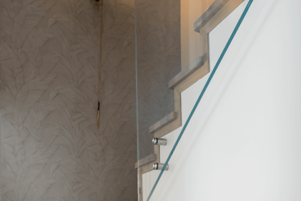 Drewniane schody ze szklaną balustradą i kinkietem na ścianie