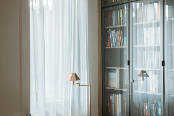 Biblioteczka za szkłem i miedziane lampy w jasnym pokoju
